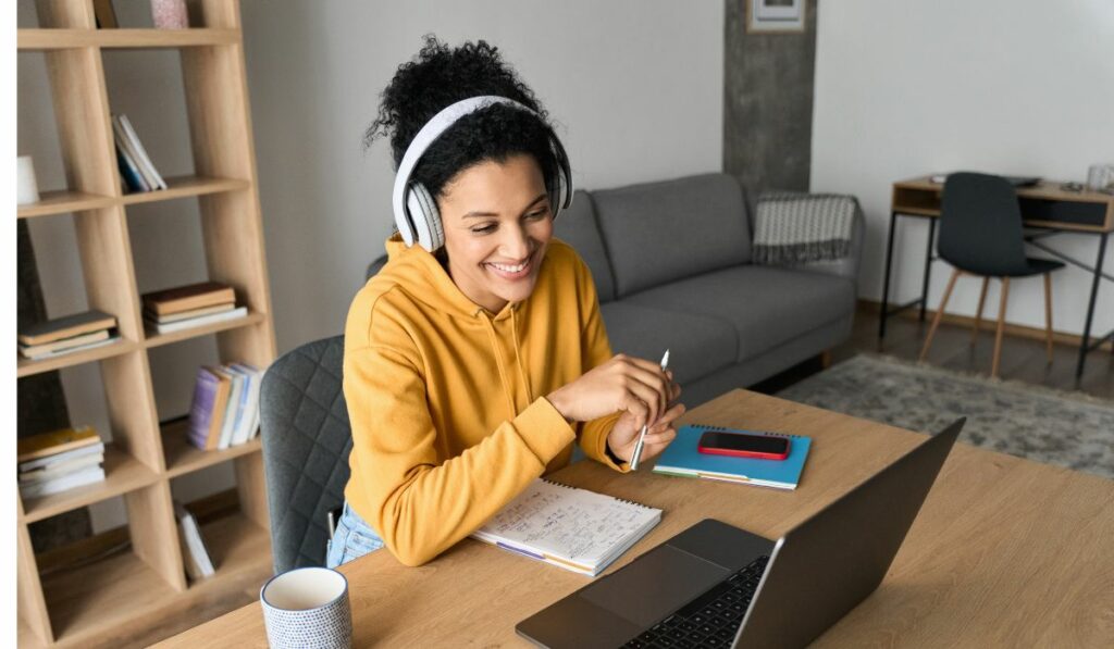 a woman taking an online side hustle course wearing a yellow sweatshirt and headphones 