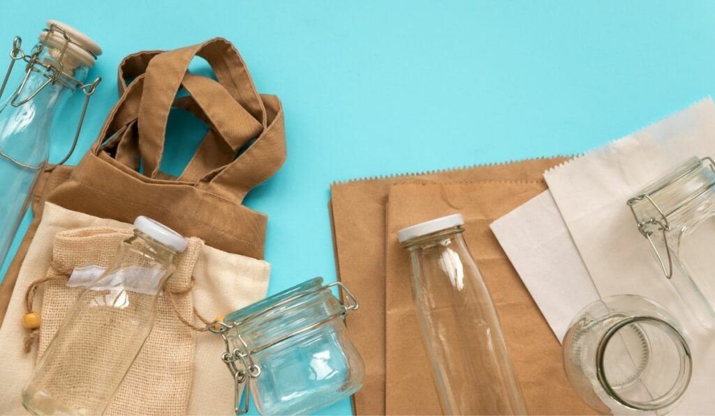 Eco-friendly items like glass jars, tote bags and to-go bags placed on a cyan background