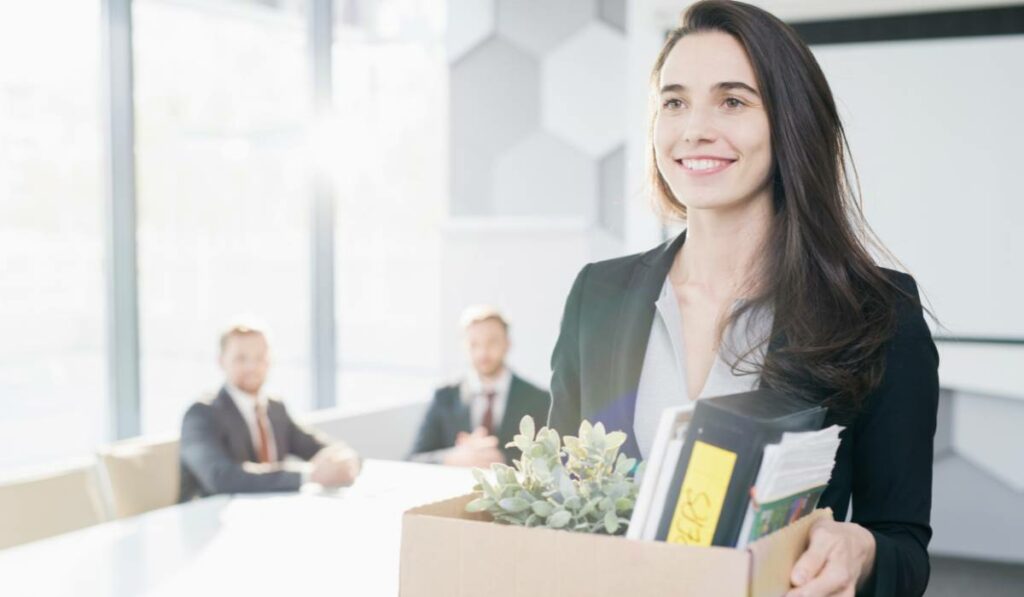 A woman in a business suit resigning from her nine to five job while holding a cardboard box full of personal items