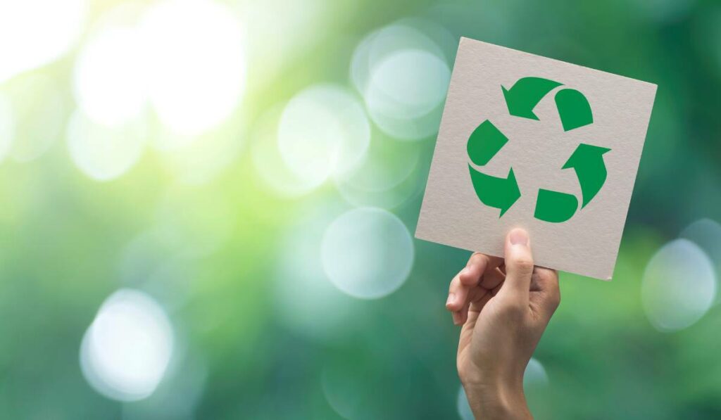 A hand holding a recycling symbol in front of a green background to show an eco-friendly initiative.