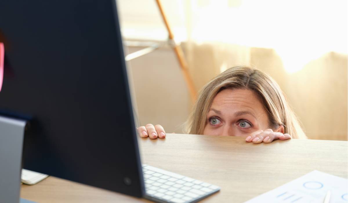 A woman peeking over a desk at a computer.
