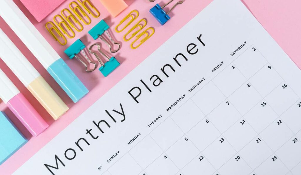 A monthly planner with office supplies on a pink background.