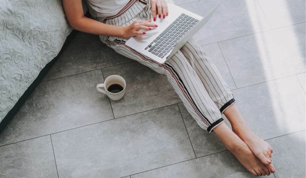 A person sitting on the floor with a laptop and a cup of coffee to work on her first high income side hustle.