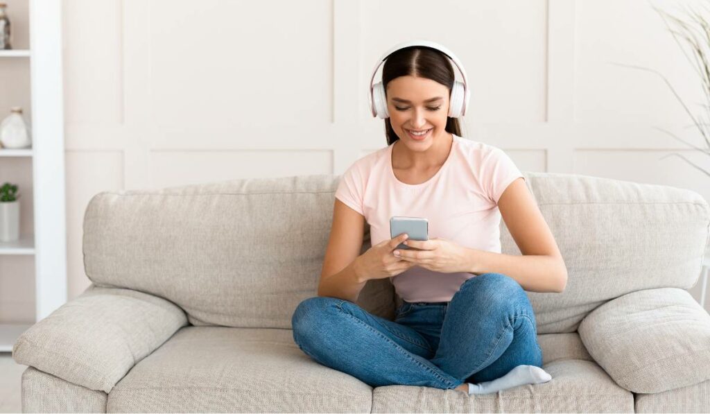 A woman is listening to a podcast on her phone while sitting on a couch