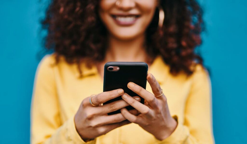 A woman with curly hair holding a cell phone while smiling