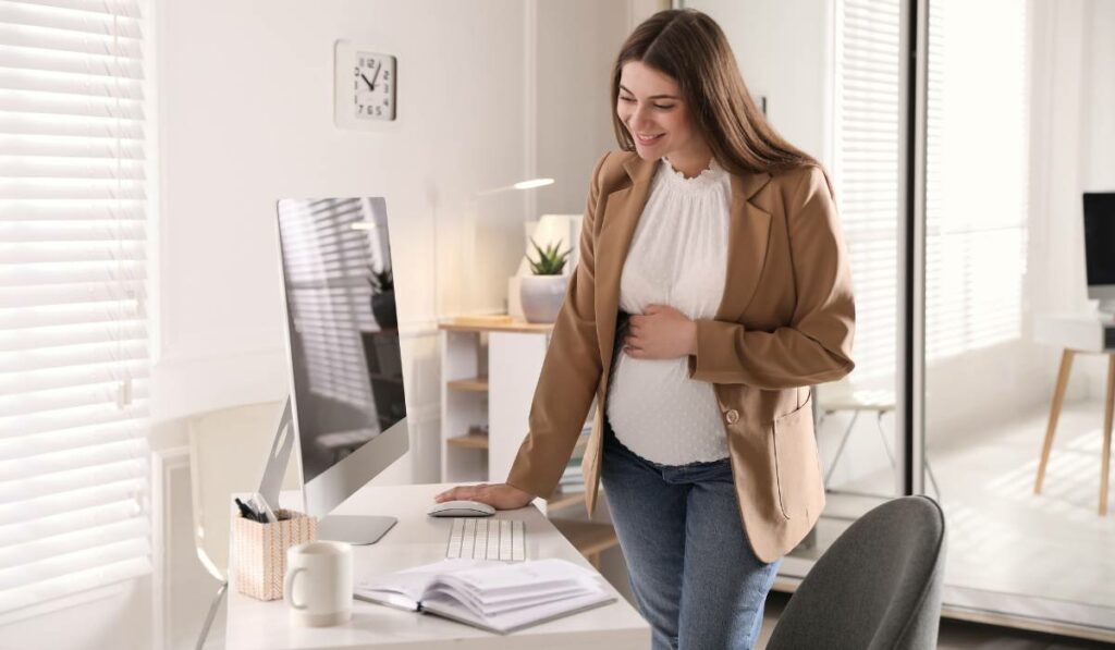 a pregnant woman smiling while standing in front of a computer