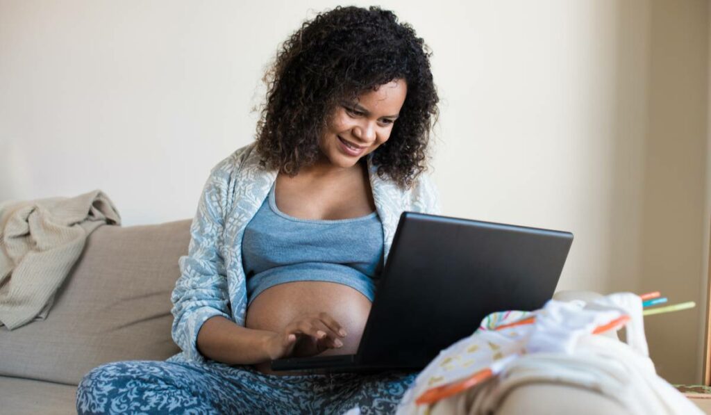 A pregnant woman smiling in front of her laptop