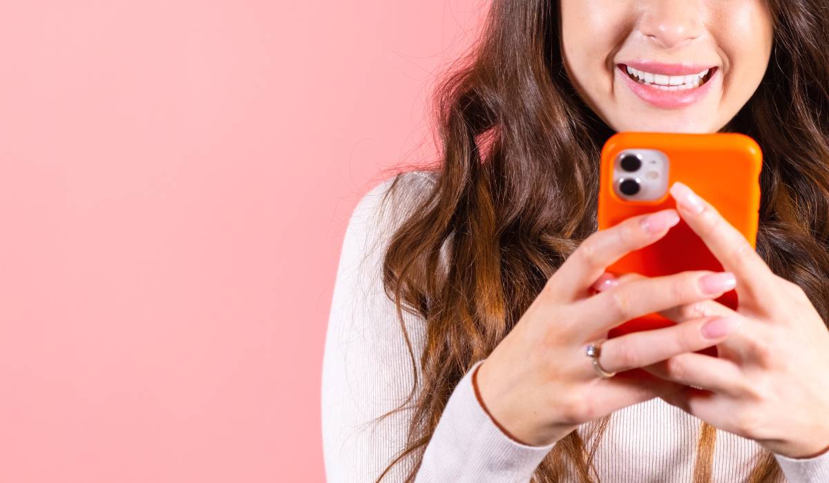 A woman smiling while holding an orange cell phone