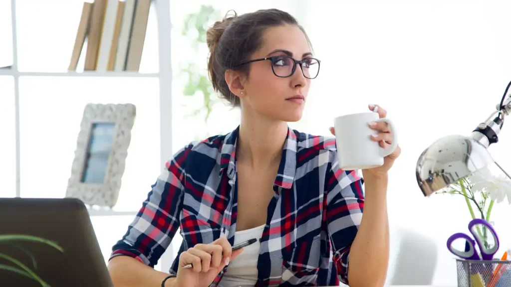 a woman is sitting at a desk with a laptop and a cup of coffee
