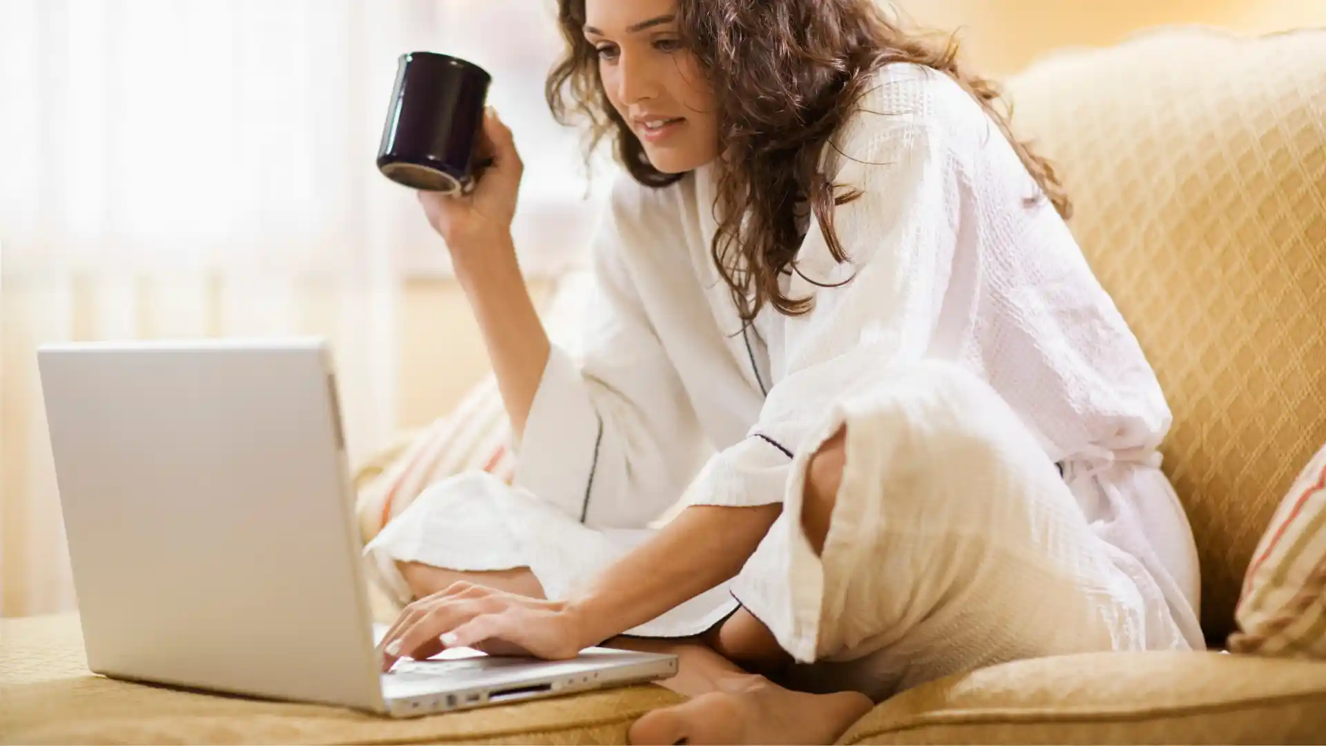 A woman sitting on a couch with a laptop and a cup of coffee